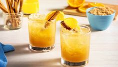 two glasses filled with orange juice and cinnamon on top of a wooden table next to blue dishes