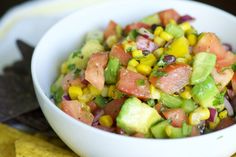 a white bowl filled with fruit and veggies next to tortilla chips