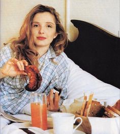 a woman sitting at a table with food and drinks in front of her on the bed