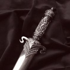 a silver colored knife with intricate designs on it's blade, resting on a black cloth