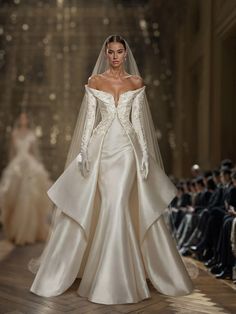 a woman in a white wedding gown and veil on the runway at a fashion show