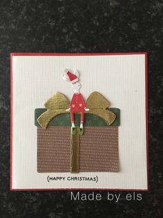 a handmade christmas card with a santa hat on top of a gift box and the words happy christmas made by els