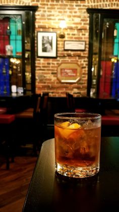 a glass filled with liquid sitting on top of a table next to a brick wall