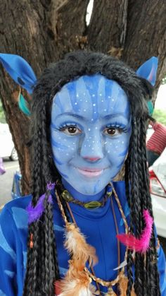 a person with blue paint on their face and long dreadlocks standing in front of a tree