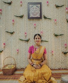 a woman sitting on the floor in front of a wall with flowers and birds hanging from it