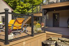 a deck with an iron railing and yellow chair on the back patio, next to a house