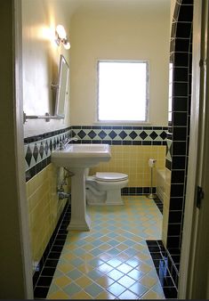 a white toilet sitting next to a sink in a bathroom under a window with yellow and black tiles