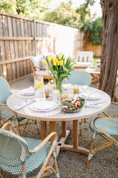 a table with plates and glasses on it in the middle of a patio area, next to a tree