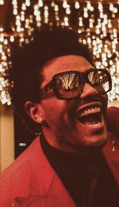 a man in a red suit and sunglasses laughing with lights on the wall behind him