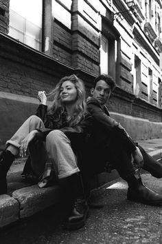 black and white photograph of two people sitting on a bench in front of a building