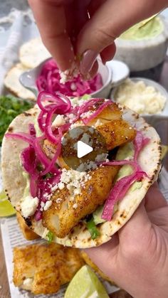 a person is holding up a taco with meat and vegetables on it, while another hand reaches for the food