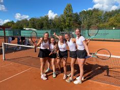 four female tennis players pose for a photo on the court with their rackets in hand