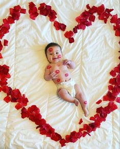 a baby laying in a heart shaped bed with petals on it's sides and his face painted red