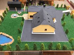 a model house is shown on top of a table with fake grass and trees around it