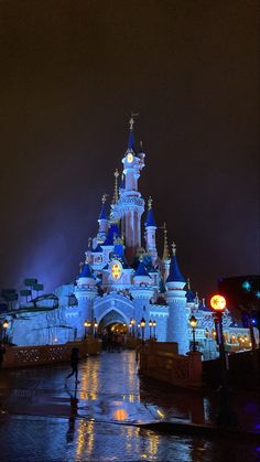 the castle is lit up at night with its lights on and people walking in front