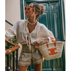 a woman wearing sunglasses and holding a basket in front of a green door with stairs