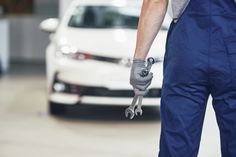 a man in overalls and gloves holding a wrench next to a white car