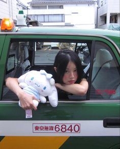 a woman sitting in the drivers seat of a green truck holding a stuffed animal and looking out the window