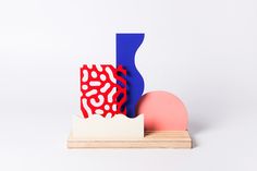 an abstract sculpture with red, white and blue shapes next to a pink ball on a wooden stand