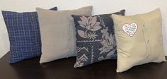 four decorative pillows are lined up on a table with a heart shaped pillow in the middle