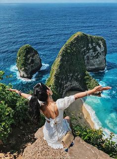 a woman standing on top of a cliff next to the ocean with her arms outstretched