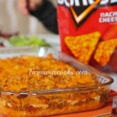 a casserole dish on a table with chips in the back ground and a bag of cheesy cheese