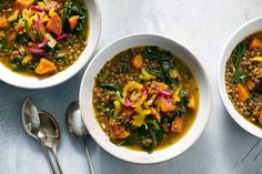 three bowls filled with lentils, carrots and other vegetables next to spoons