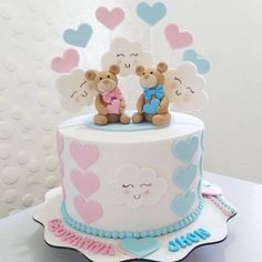 two teddy bears sitting on top of a white and blue cake with hearts in the background