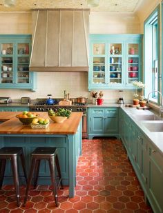 a kitchen with blue cabinets and wooden counter tops, red tile flooring and an island in the middle