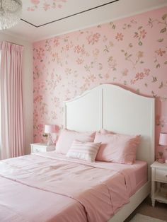 a bedroom decorated in pink and white with flowers on the wall, bedding and curtains