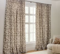 a living room with a couch, chair and window covered in drapes next to a white rug