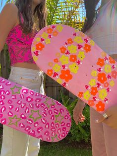 two women holding skateboards in their hands and one is wearing a pink top with flowers on it