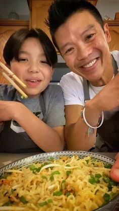 two people posing for the camera with some food in front of them and chopsticks sticking out of their mouths