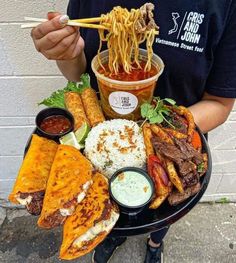 a man is holding a plate full of food and dipping sauces on the side