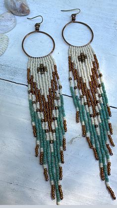 S o o r a j   earrings were handcrafted using colors matte cream, gold luster, Picasso turquoise and bronze with high quality Japanese seed beads. Suspended from hand crafted  antique brass hoops using quality Japanese nylon thread for durability. These come with silicone encapsulated antique brass backs to secure your earrings. Nickel and lead free. *LAST PICTURE IS FOR SIZE REFERENCE ONLY * Fringes swing beautifully and are light weight.  **Please care for your jewelry as you would with any va White Beaded Fringe Jewelry For Crafting, White Bohemian Fringe Earrings, Handmade Southwestern Gold Earrings, Bohemian Brown Hoop Earrings, Brown Bohemian Hoop Earrings, Artisan White Fringe Jewelry, Beige Bohemian Fringe Earrings, Handmade White Bohemian Tassel Earrings, White Bohemian Jewelry With Dangling Beads