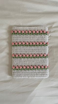 a crocheted square with pink roses on it sitting on a white bed sheet