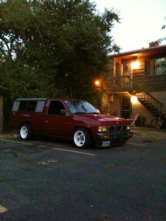 a red pick up truck parked in front of a house at night with its lights on