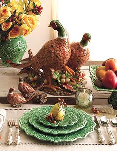 a table topped with green plates covered in turkey figurines next to vases filled with flowers