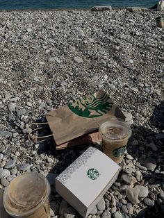 starbucks coffee and book on rocky beach next to water