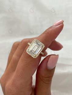 a woman's hand holding an engagement ring with a large emerald stone surrounded by small diamonds