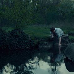 a man standing on top of a river next to a lush green forest filled with trees