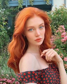 a woman with red hair and blue eyes posing in front of flowers