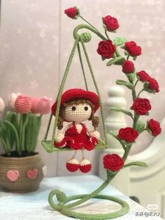 a crocheted doll sitting on a swing with flowers in the background