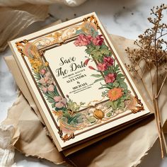 a wedding card with flowers on it next to some dried plants and paper wrappings