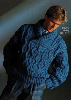 a man wearing a blue cabled sweater and pants with his hands on his hips