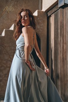 a woman in a blue dress leaning against a wall