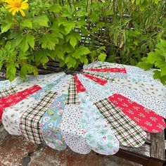 a quilted tablecloth is sitting on a wooden bench in front of some plants