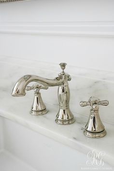 two chrome faucets sitting on top of a white marble countertop in a bathroom