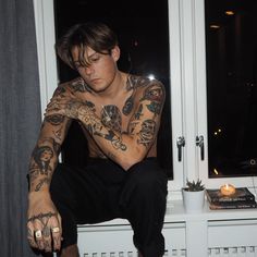 a man with tattoos sitting on a window sill