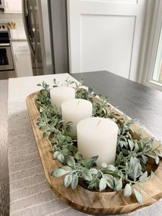 three candles sitting on top of a wooden tray filled with greenery and eucalyptus leaves